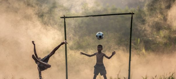 crianaça jogando futebol no campo cheio de água