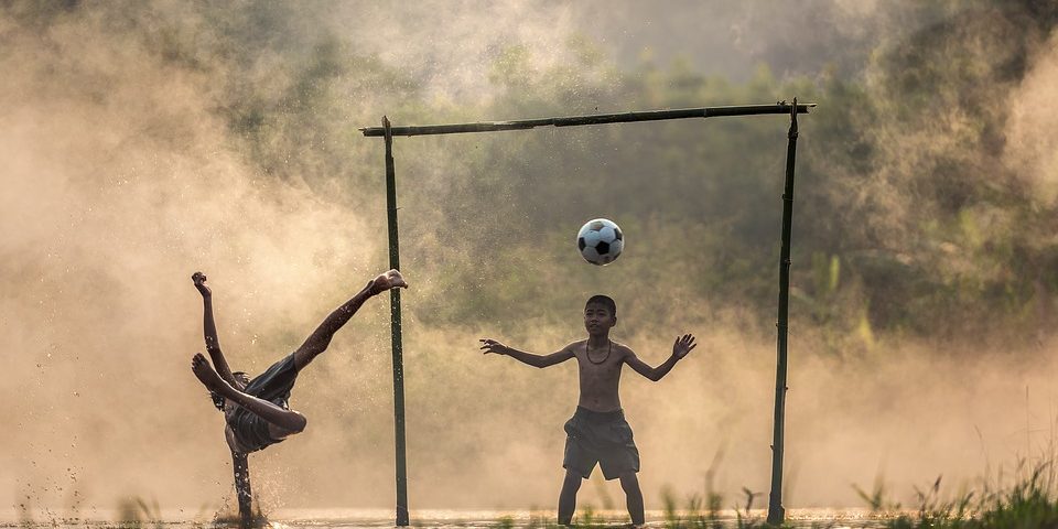 crianaça jogando futebol no campo cheio de água